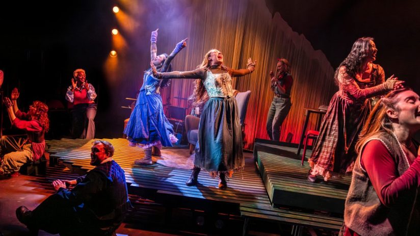 The ensemble of Ballad Lines performing on stage, captured by Pamela Raith, showcasing dynamic expressions and vibrant cos...