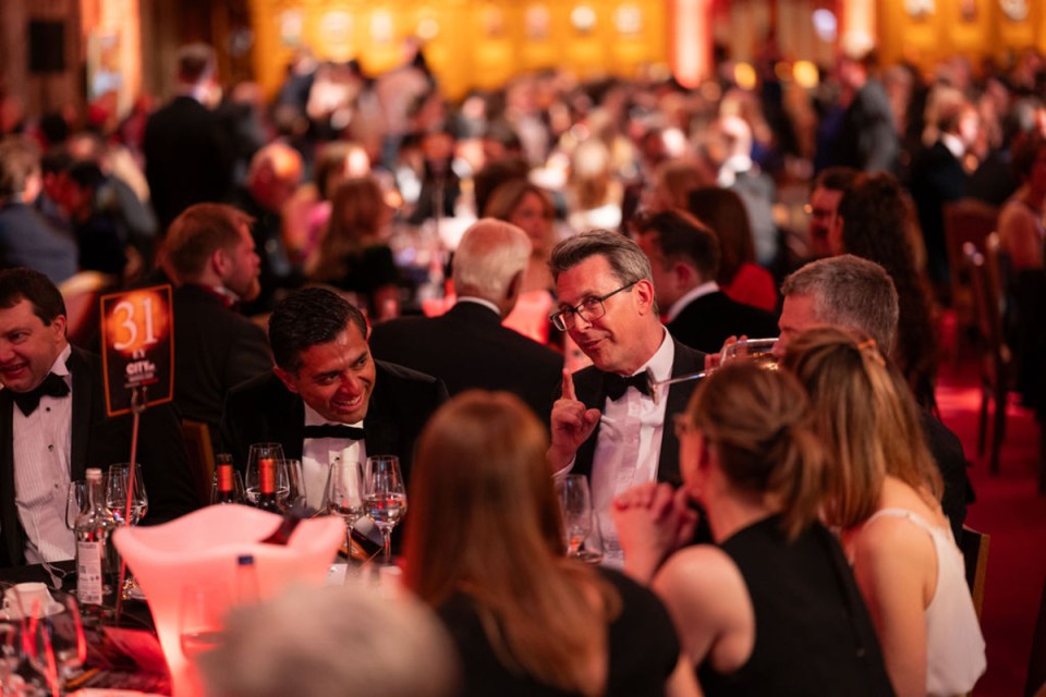 CityAM Awards atmosphere with elegant gala setting, attendees in formal attire, glittering lights, and award stage in the...