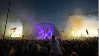 Aerial view of Glastonbury Festival showcasing vibrant crowds, colorful tents, and iconic Pyramid Stage under clear skies