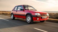 Vintage Peugeot 205 driving on a scenic road, showcasing classic design and compact size for a news feature on iconic cars