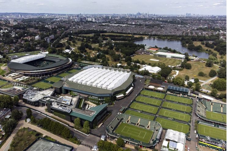 Wimbledon tennis court with players in action, surrounded by a cheering crowd under clear blue skies