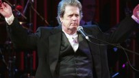 Brian Wilson performing live on stage, surrounded by musical instruments and colorful stage lights, captivating the audience