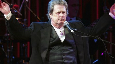 Brian Wilson performing live on stage, surrounded by musical instruments and colorful stage lights, captivating the audience