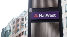 NatWest sign on a dark pillar with vertical slats, set against a blurred background of a modern office building