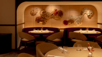 Elegant restaurant interior with round tables, plush burgundy booths, and textured floral wall art