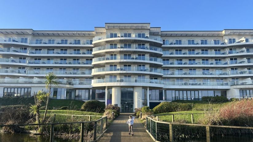 Modern Butlins hotel building with multiple balconies, a path leading to it, and a small pond in the foreground.