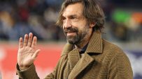 Andrea Pirlo, former Italian footballer, waving to the crowd in a brown tweed coat.