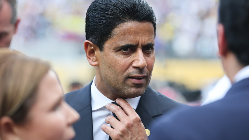 Nasser Al-Khelaifi adjusting his tie, speaking to another person in a business setting