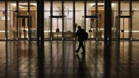 Silhouetted person walks past a modern building with 10 Upper Bank Street visible on its glass facade at night.