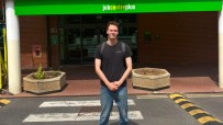 Young man in front of a Jobcentre Plus building, standing on a pedestrian crossing.