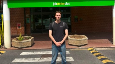 Young man in front of a Jobcentre Plus building, standing on a pedestrian crossing.