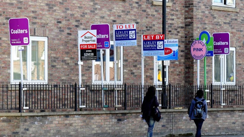 Numerous For Sale and To Let signs from various real estate agents outside a brick building.