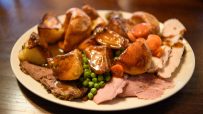 Close-up of a plated roast dinner with meat, roasted potatoes, peas, carrots, and gravy on a white plate