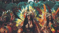 Three revelers in vibrant feathered costumes celebrating at Notting Hill Carnival.