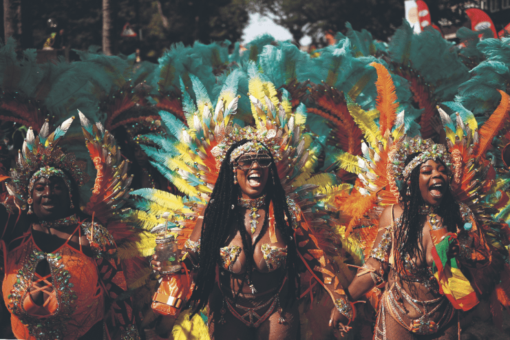Three revelers in vibrant feathered costumes celebrating at Notting Hill Carnival.