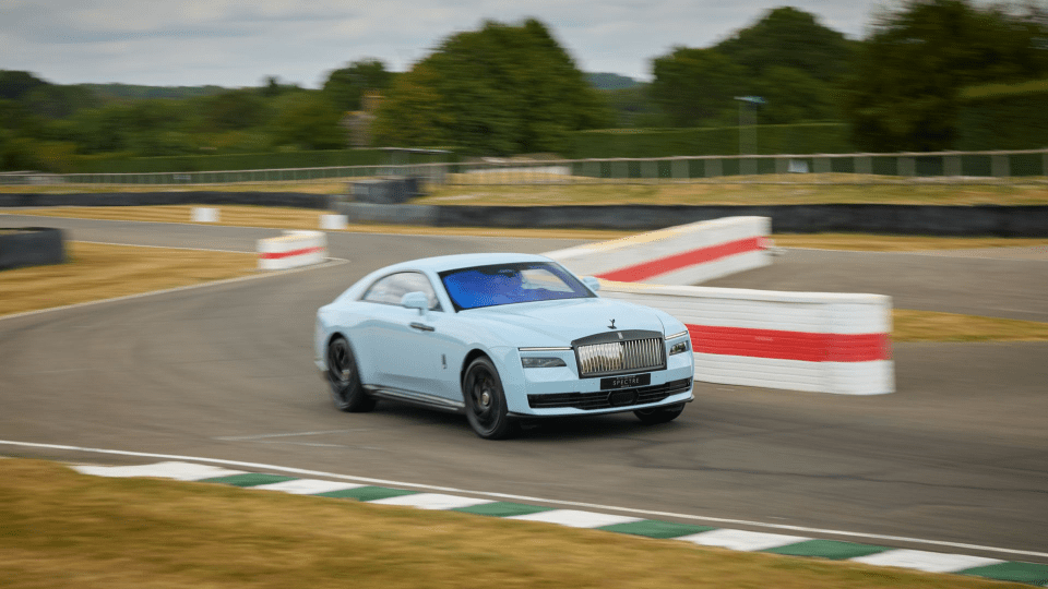 Light blue Rolls-Royce Spectre electric car on a race track with motion blur.