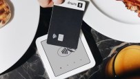 Hand holding black SumUp payment card over a white contactless reader on a marble table with breakfast food