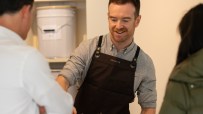 Smiling barista wearing a ROSSLYN apron serving a customer at a coffee shop counter.